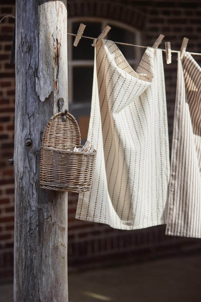 A tea towel hanging from a washing line in the sun. The towel is cream with a brown interwoven stripe pattern.