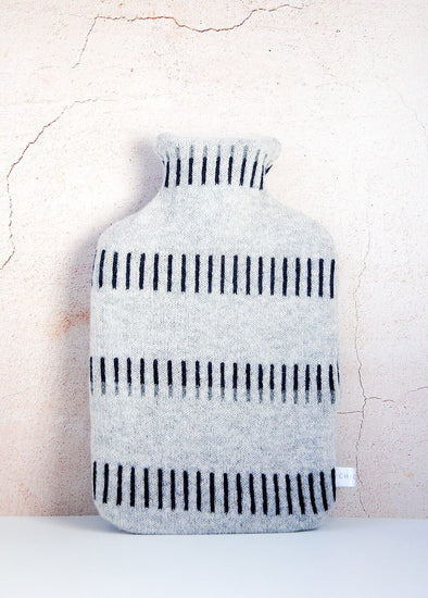 Light grey knitted lambswool hot water bottle with a navy blue dash pattern. Height thirty four centimetres, width twenty centimetres.