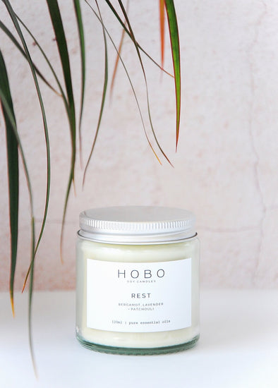Aromatherapy travel candle, handmade by HoBo Soy Candles using one hundred percent essential oils. The label shows the scent as being bergamot, lavender and patchouli. The candle is presented in a one hundred and twenty millilitre recycled clear glass jar with a metal lid. The jar is six centimetres high and five point five centimetres wide.
