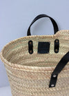 Close up of a basket bag with short black leather handles.