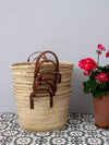 Stack of basket bags with short tan leather handles sitting next to a red geranium in a terracotta pot.