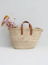 Basket bag with short tan leather handles. Some pink and orange flowers rest inside the bag.
