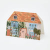 Greetings card in the shape of a house. It has a pale pink door, sky blue window frames and a red tiled roof. Lots of flowers and greenery grow infront and up the walls.