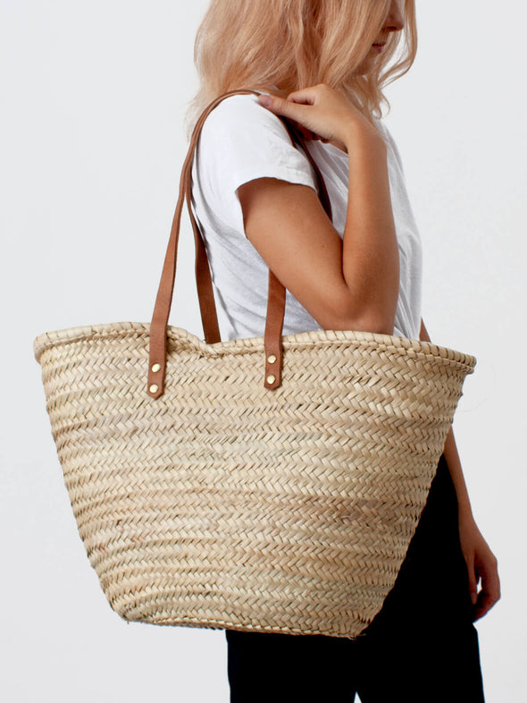Woman with a basket bag with long tan leather straps on her shoulder.