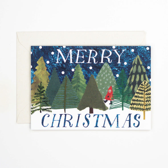 Greetings card depicting a snowy woodland scene with a person in a red cape walking through the trees. Text reads Merry Christmas.