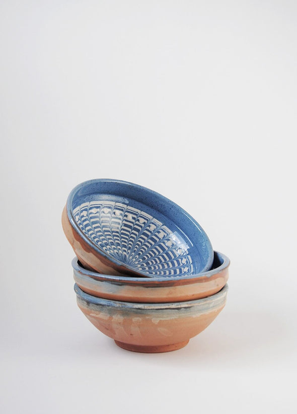 Stack of three ceramic bowls decorated in traditional Romanian pattern. Blue base with swirls of white.