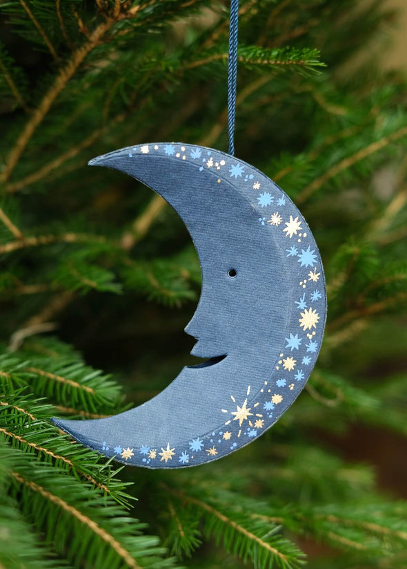 Decorative blue moon ornament with star patterns hanging on a tree.