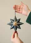 Hand holding a blue star-shaped ornament against a neutral background