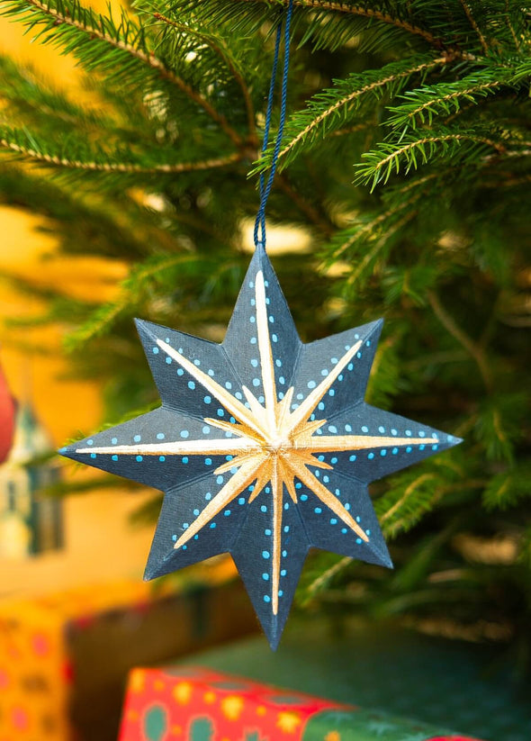 Decorative star ornament hanging on a Christmas tree with blurred gift boxes in the background.
