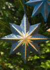 Decorative star ornament with blue and gold patterns, hanging on a tree.
