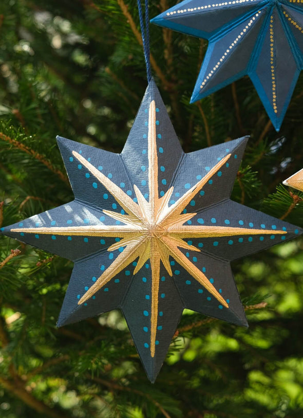 Decorative star ornament with blue and gold patterns, hanging on a tree.