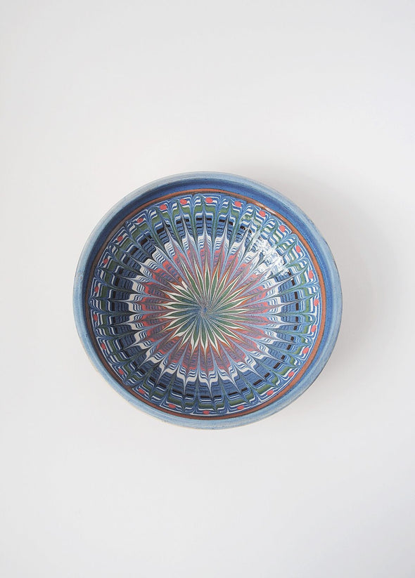 Ceramic bowl decorated in traditional Romanian pattern. Blue base with swirls of white, red, yellow, black and green.