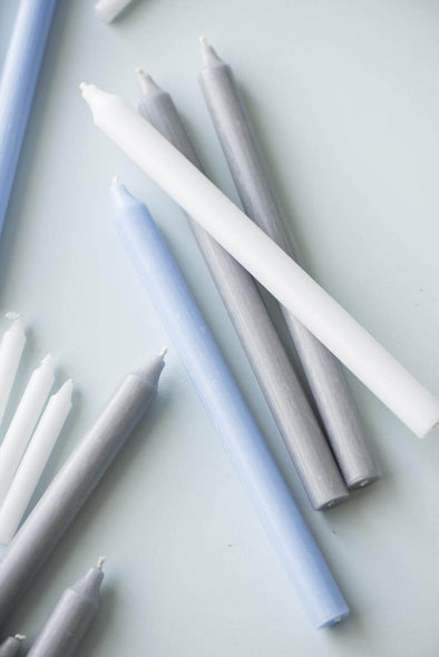 A selection of long dinner candles randomly lying about. It is a mix of white, light grey and light blue candles.
