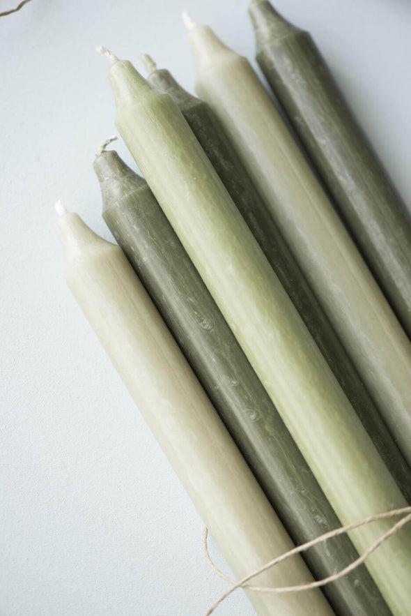 A close up of a selection of dinner candles. It is a mix of light green and dark green candles.