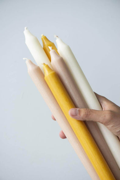 A hand holding a selection of dinner candles. It is a mix of yellow, beige and white candles.