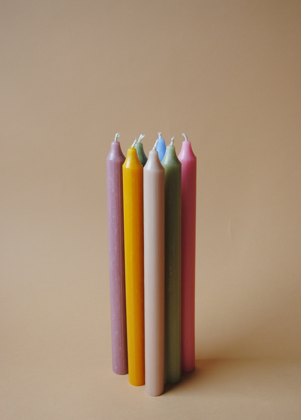 Seven long dinner candles in different colours standing upright in a group.