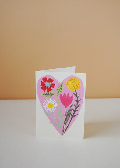 Greetings card with a painted image of a selection of wild flowers inside a pink heart.