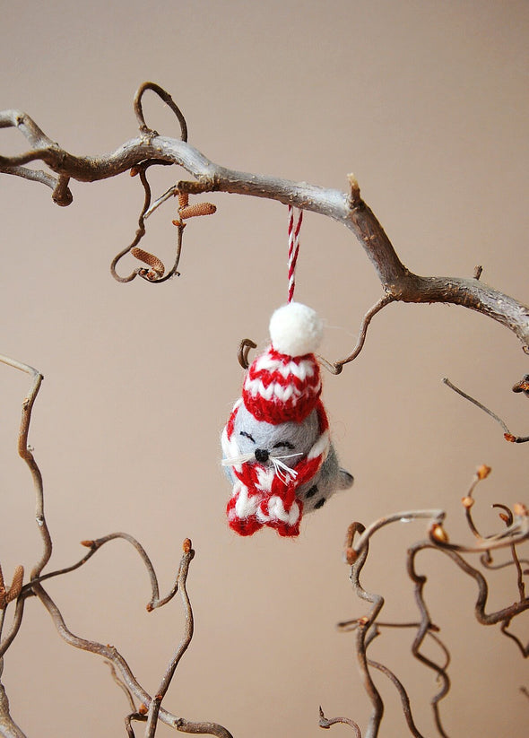 Decorative ornament of a seal with a red and white striped hat and scarf, hanging from a branch.
