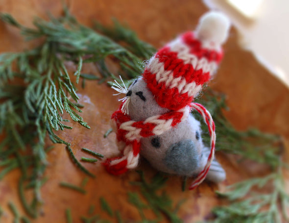 Small seal ornament with a red and white striped hat and scarf on a wooden surface with greenery