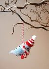 Wool seal decoration wearing a knitted hat and scarf, hanging from a branch against a beige background