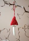 Red and white mushroom ornament hanging from a branch against a neutral background
