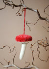 Red and white mushroom ornament hanging from a branch against a beige background