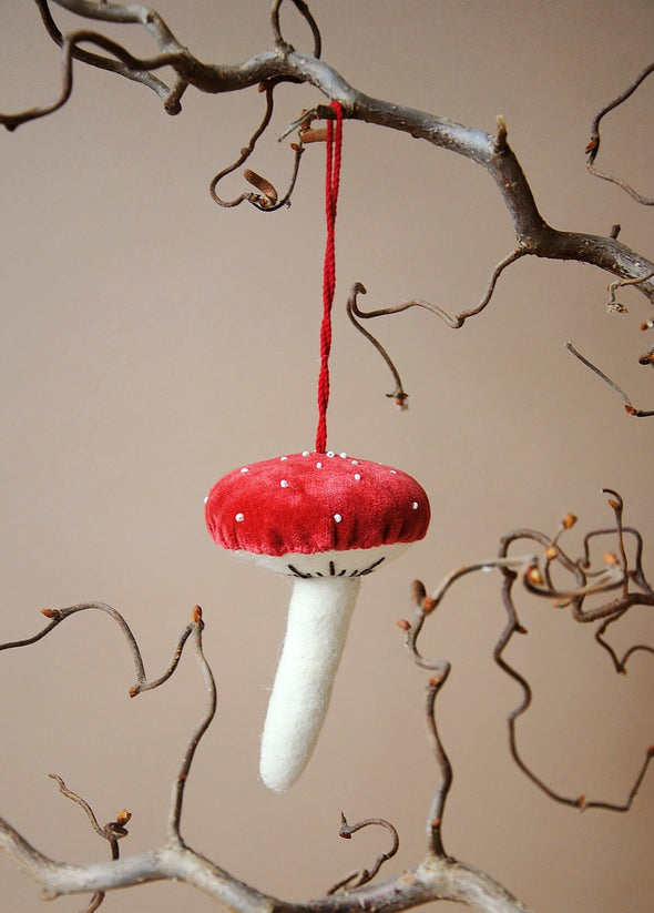 Red and white mushroom ornament hanging from a branch against a beige background