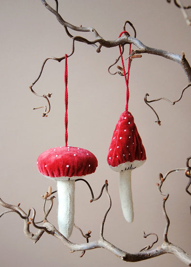 Two red and white mushroom-shaped ornaments hanging from a branch against a neutral background.