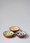 Three ceramic small bowls. One has a white glaze with blue splatter pattern on interior, the second has a white glaze with yellow and orange splatter pattern on interior and the third has a while glaze with green splatter pattern on interior. All have a terracotta glaze on exterior.