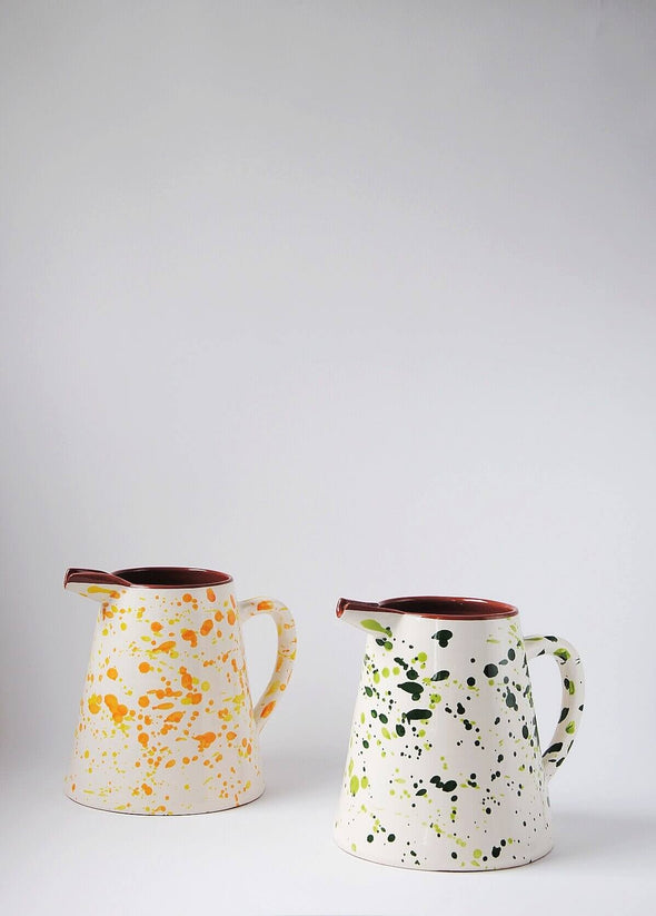 Two ceramic large jugs. One has a white glaze with green splatter pattern on exterior, and the other a white glaze with orange and yellow splatter pattern on exterior. Both have a terracotta glaze on interior.