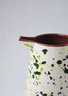 Close up of ceramic large jug. White glaze with green splatter pattern on exterior, terracotta glaze on interior.