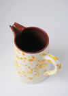 Ceramic large jug. White glaze with orange and yellow splatter pattern on exterior, terracotta glaze on interior.
