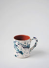 Ceramic mug with handle. White glaze with blue splatter pattern on exterior, terracotta glaze on interior.