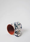 Ceramic mug with handle, lying on its side. White glaze with blue splatter pattern on exterior, terracotta glaze on interior.