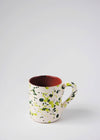 Ceramic mug with handle. White glaze with green splatter pattern on exterior, terracotta glaze on interior.
