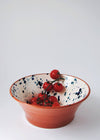 Ceramic salad bowl. White glaze with blue splatter pattern on interior and terracotta glaze on exterior. Tomatoes on a vine rest in the bowl.