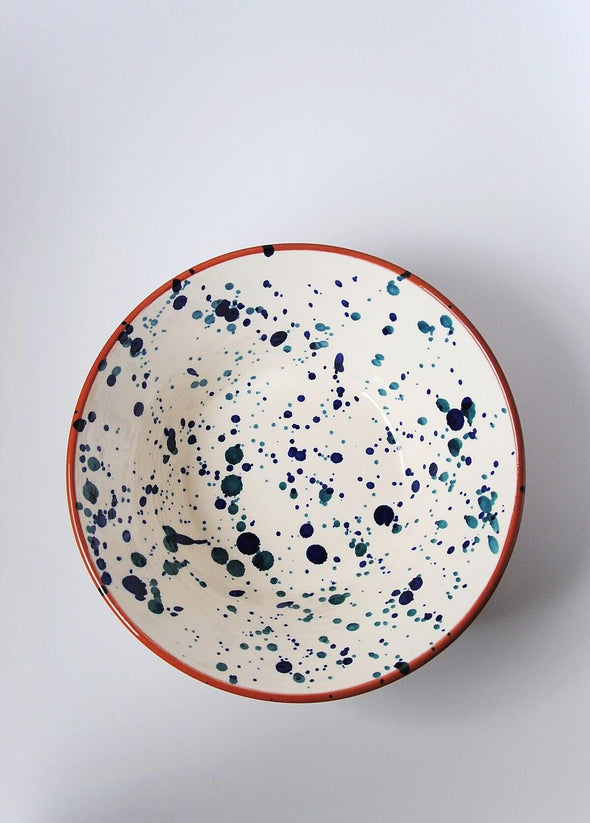Ceramic salad bowl from above. White glaze with blue splatter pattern on interior and terracotta glaze on exterior.