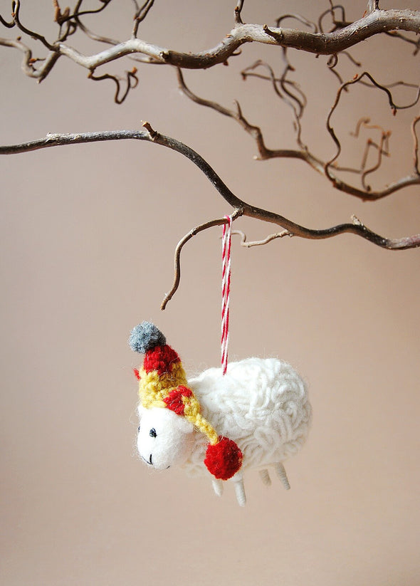 Wool sheep decoration with a colourful hat hanging on a branch against a neutral background
