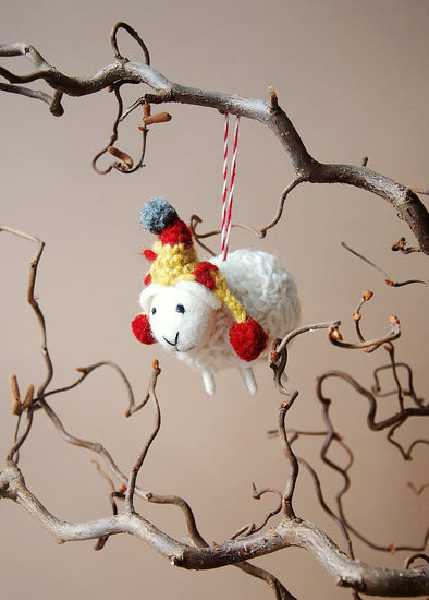 Wool sheep decoration with a colourful hat hanging on a branch against a neutral background