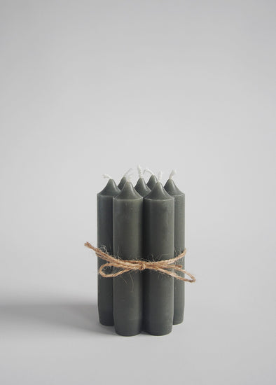 A group of seven dark green dinner candles tied together with twine.
