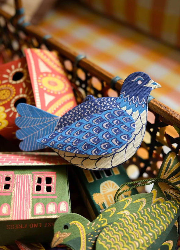 A box of decorations. On the top sits a blue dove decoration next to a green partridge decoration.