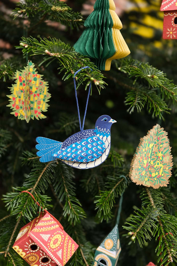 Mixed decorations hanging on a Christmas tree. Some are paper trees, some honeycomb trees and in the middle is a blue dove made from paper board and printed in a detailed blue pattern.