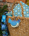 Blue paper chain hanging down the side of a basket. A dove hanging decoration made from card and painted in a detailed blue pattern, hangs from the side of the basket. A gift wrapped in blue paper with a blue and yellow star pattern rests in the basket.