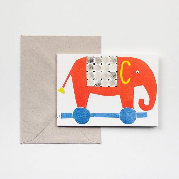 Greetings card depicting a red toy elephant on blue wheels.