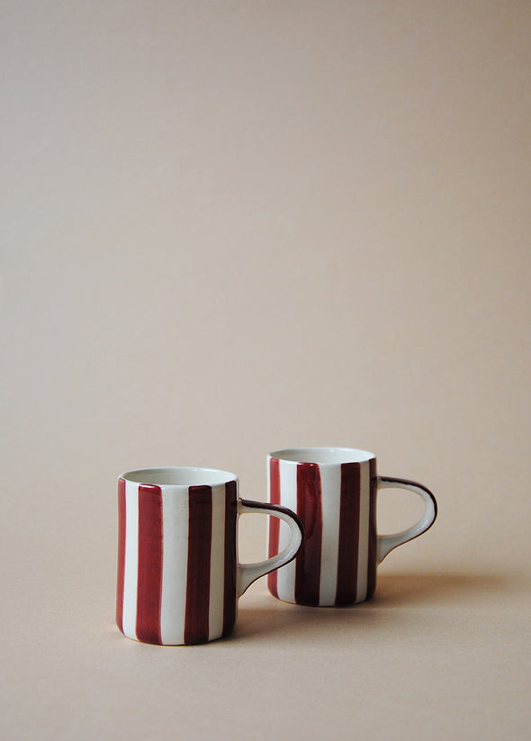 Two burgundy and white striped ceramic espresso cups sitting side by side.