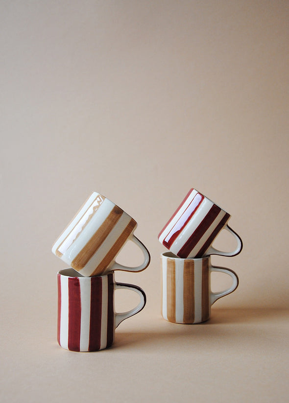 Two stacks of two espresso cups. Each stack has one light brown and white striped cup and one burgundy and white striped cup.