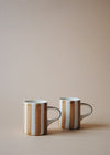 Two light brown and white striped ceramic espresso cups sitting next to each other.