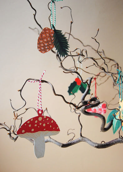 Five assorted gift tags each with a loop of string attached. Each tag is a picture and shape of a toadstool, sprig of holly, pine cone, red berries and yellow berries. They are all hanging off curly branches.