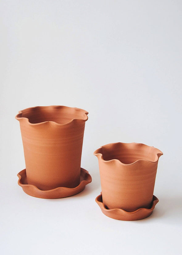 Two terracotta planters and saucers, one large and one small. Both planter and saucer have a frilly edge.