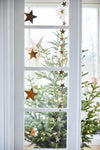 String of brass stars handing down a window with a Christmas tree in the background.